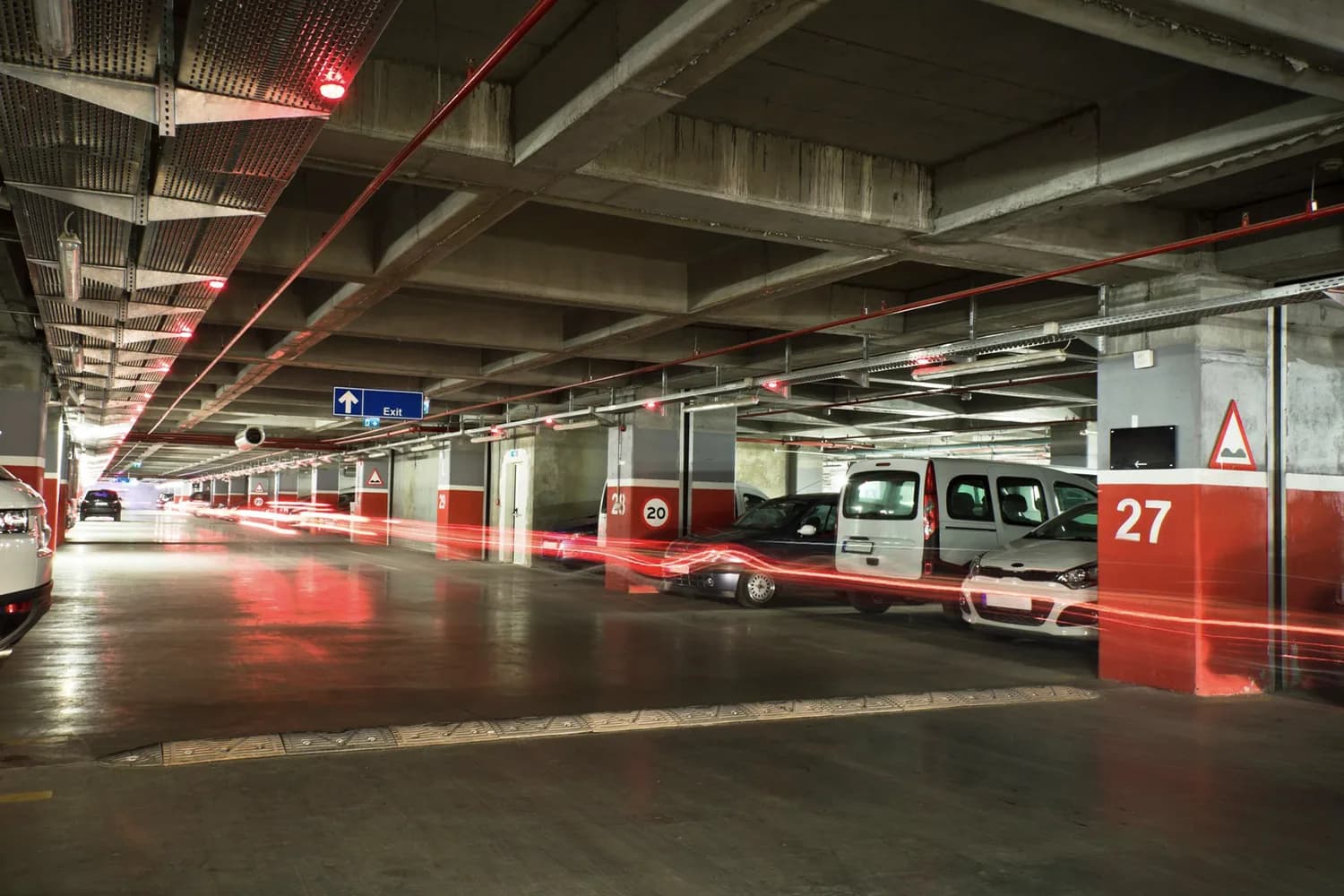 Parkdeck in Tiefgarage mit geparkten Fahrzeugen, Exit-Schild und roten Lichtspuren durch Langzeitbelichtung