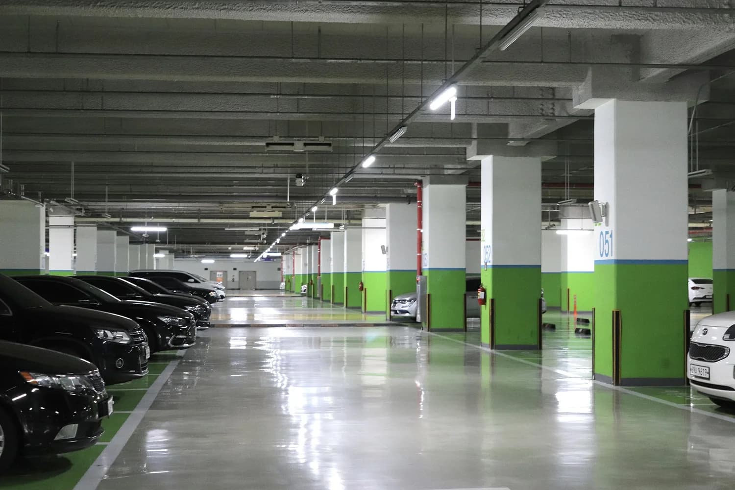 Tiefgarage mit grün markierten Stellplätzen, nummerierten Säulen und beleuchteter Fahrgasse voller geparkter Autos