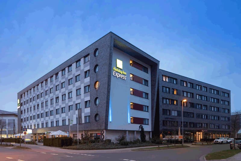 Mehrstöckiges Hotelgebäude mit Holiday Inn Express Leuchtschrift und beleuchteten Fenstern bei Dämmerung.
